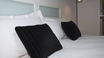 A hotel room with a bed, white bedding, and black pillows.