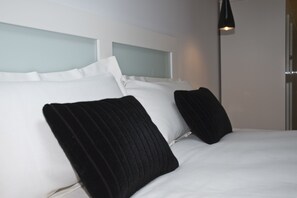 Une chambre d’hôtel avec un lit, du linge de lit blanc et des oreillers noirs.
