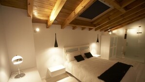 Een slaapkamer met een houten plafond, een bed met witte lakens, een nachtkastje en een vloerlamp.