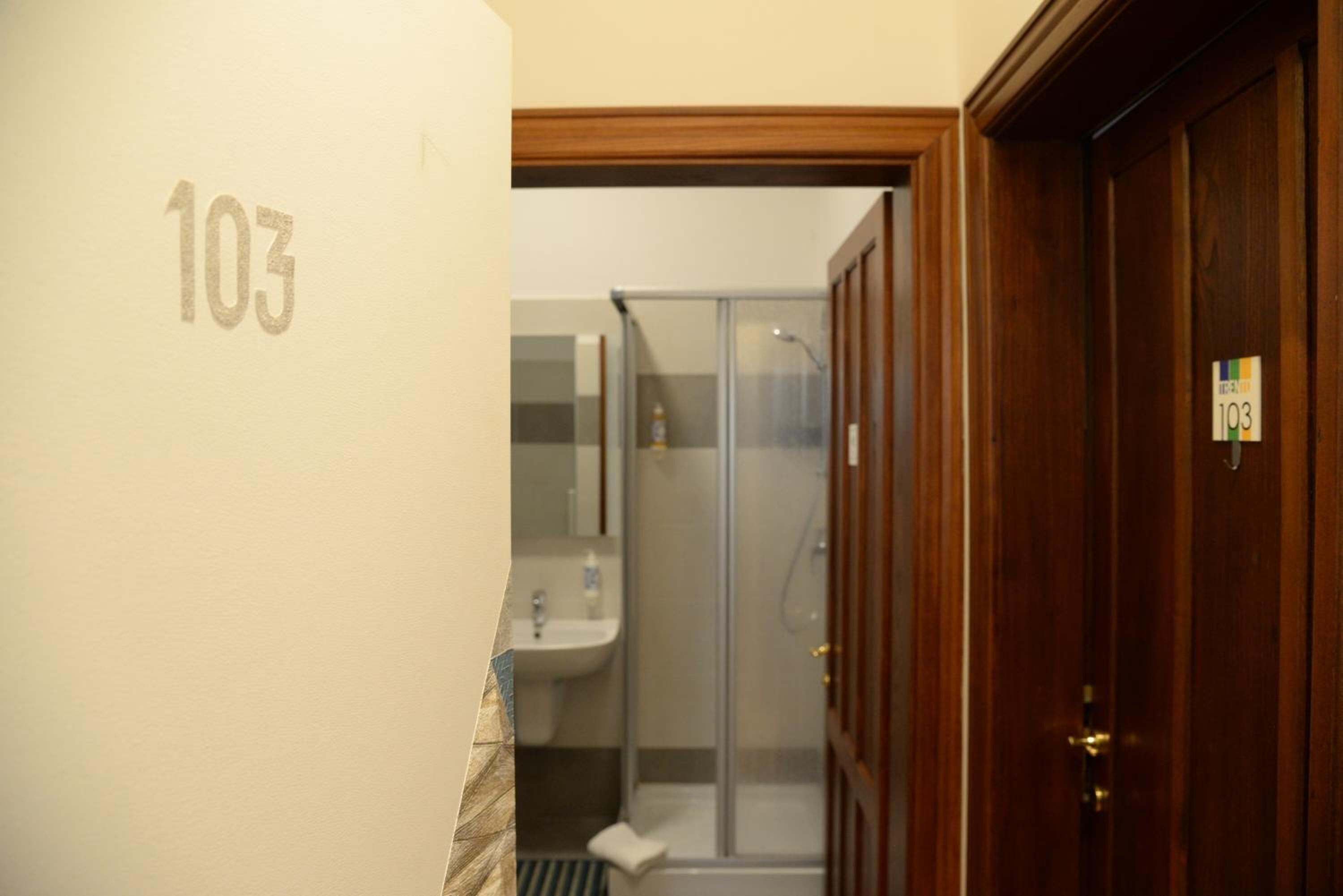 Un baño con ducha, lavamanos y una puerta con la etiqueta '103'.