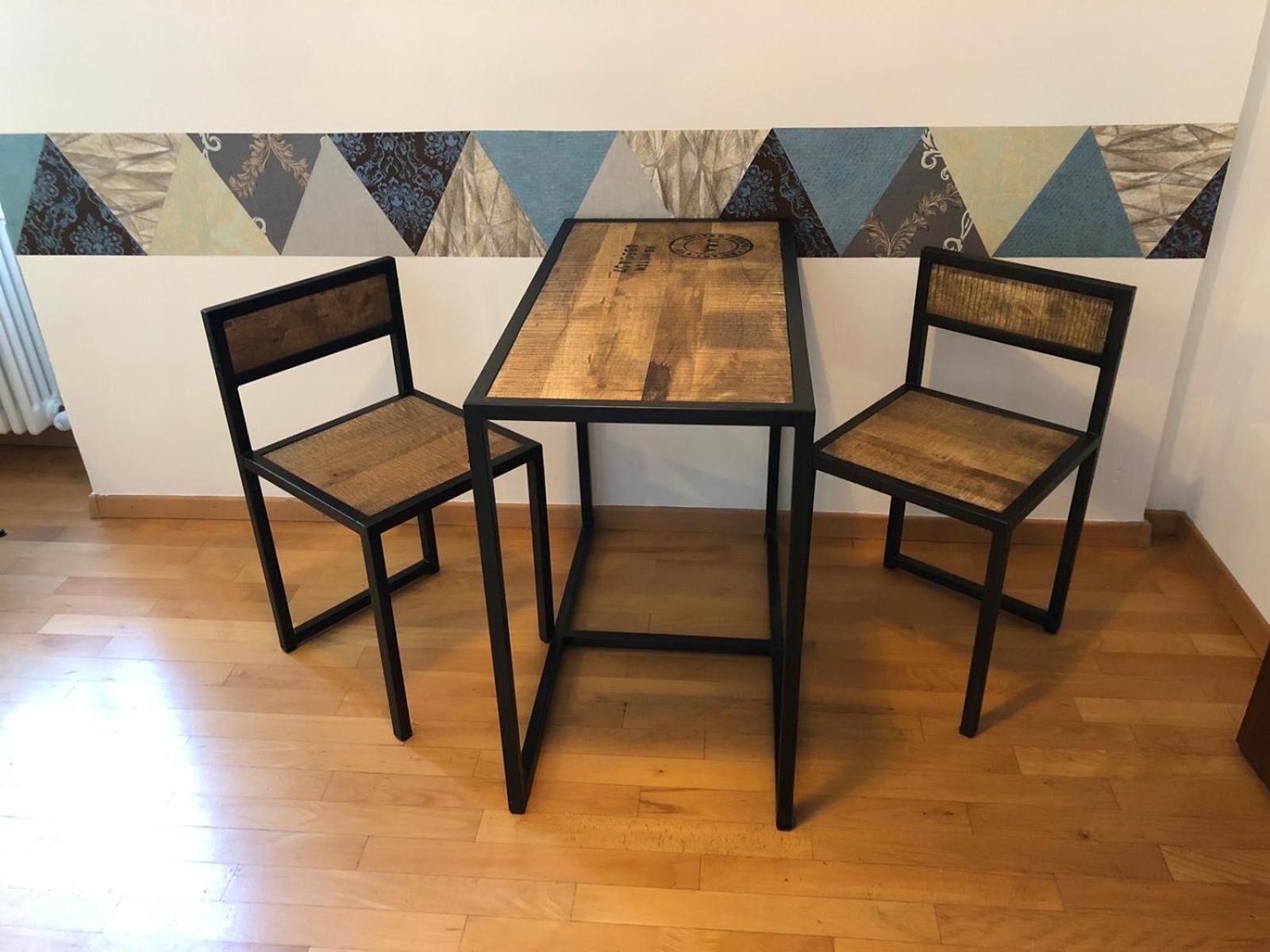En matplats med ett träbord och två stolar, placerad framför en vägg med ett geometriskt mönster.