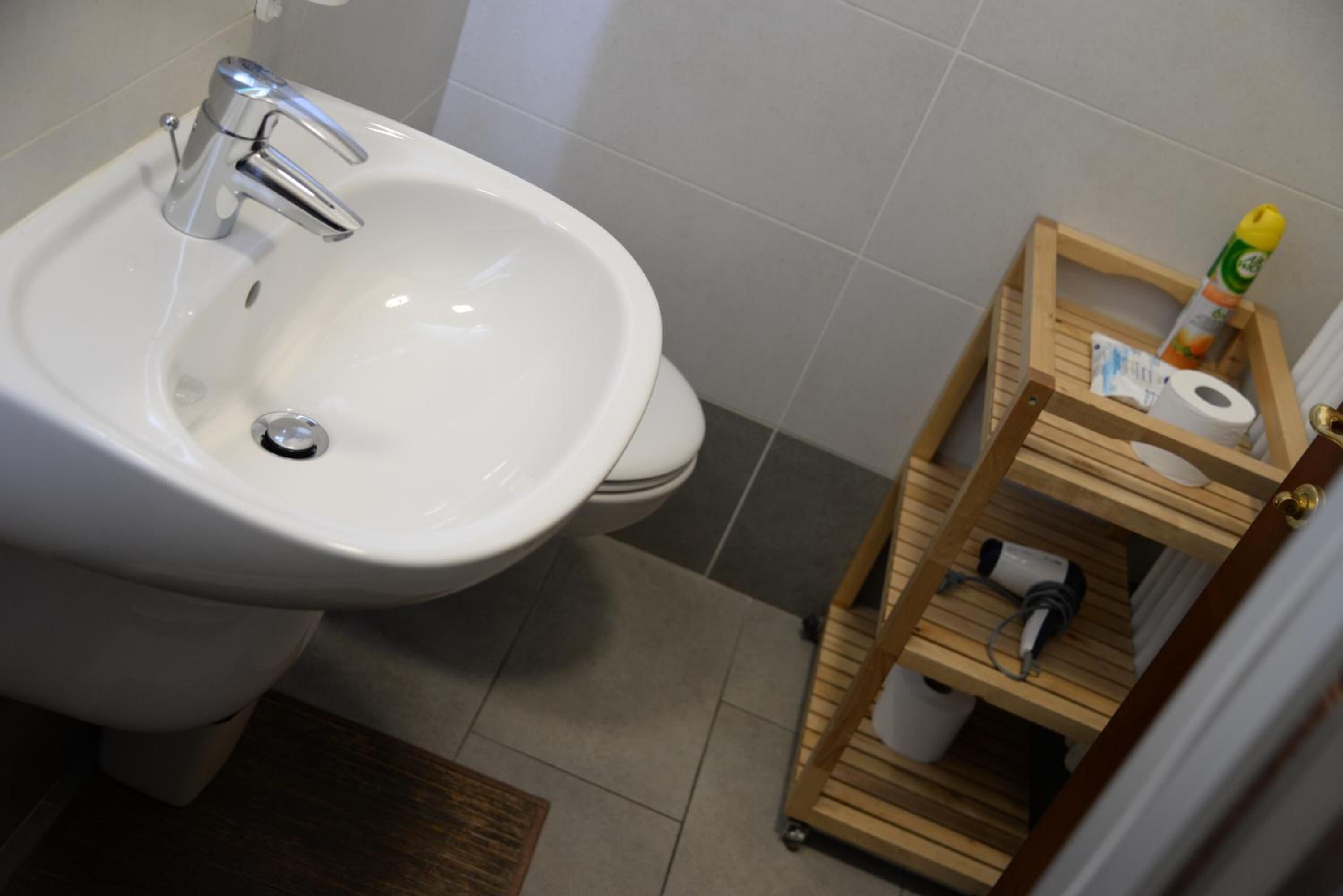 A bathroom with a white sink, a wooden shelf with toiletries, and a toilet.