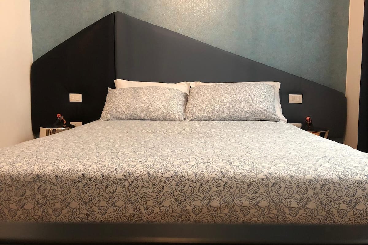 A bed with a floral-patterned bedspread and two pillows, a dark headboard, and a light blue wall.