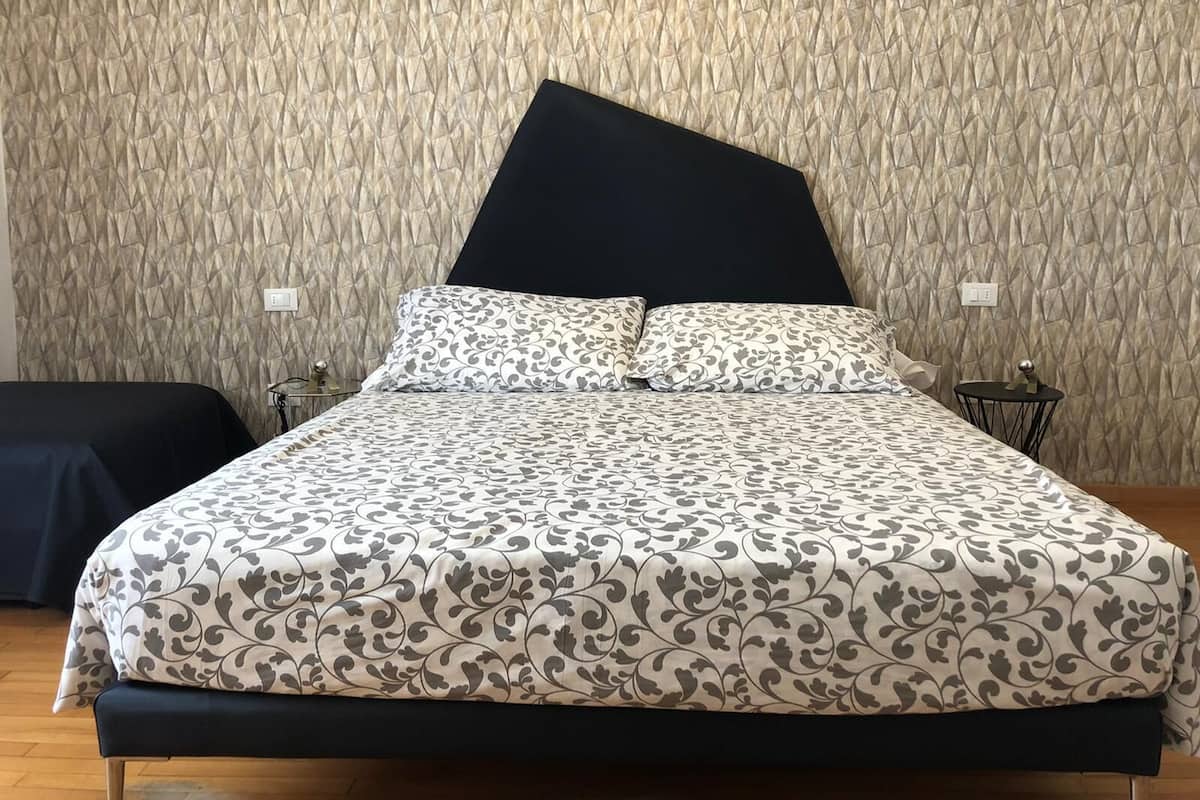 A bed with a patterned bedspread, a black headboard, and two bedside tables with lamps.