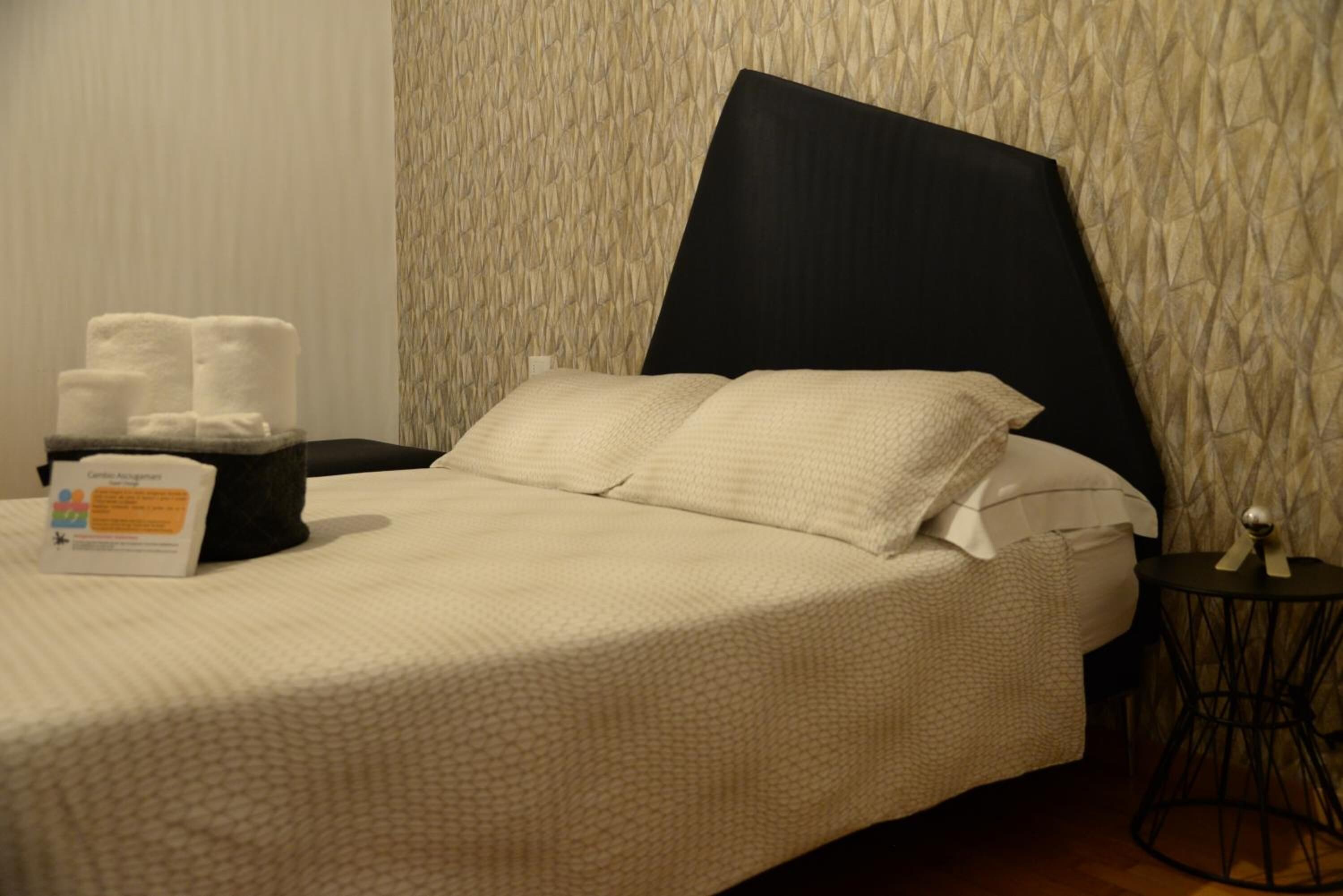 A neatly made bed with a large pillow and a bedside table with a tissue box and towels.