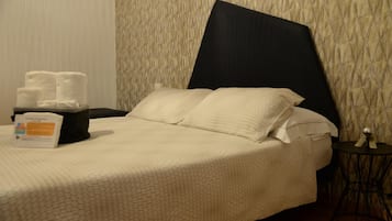 A neatly made bed with a large pillow and a bedside table with a tissue box and towels.