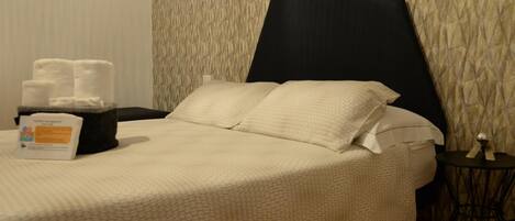 A neatly made bed with a large pillow and a bedside table with a tissue box and towels.