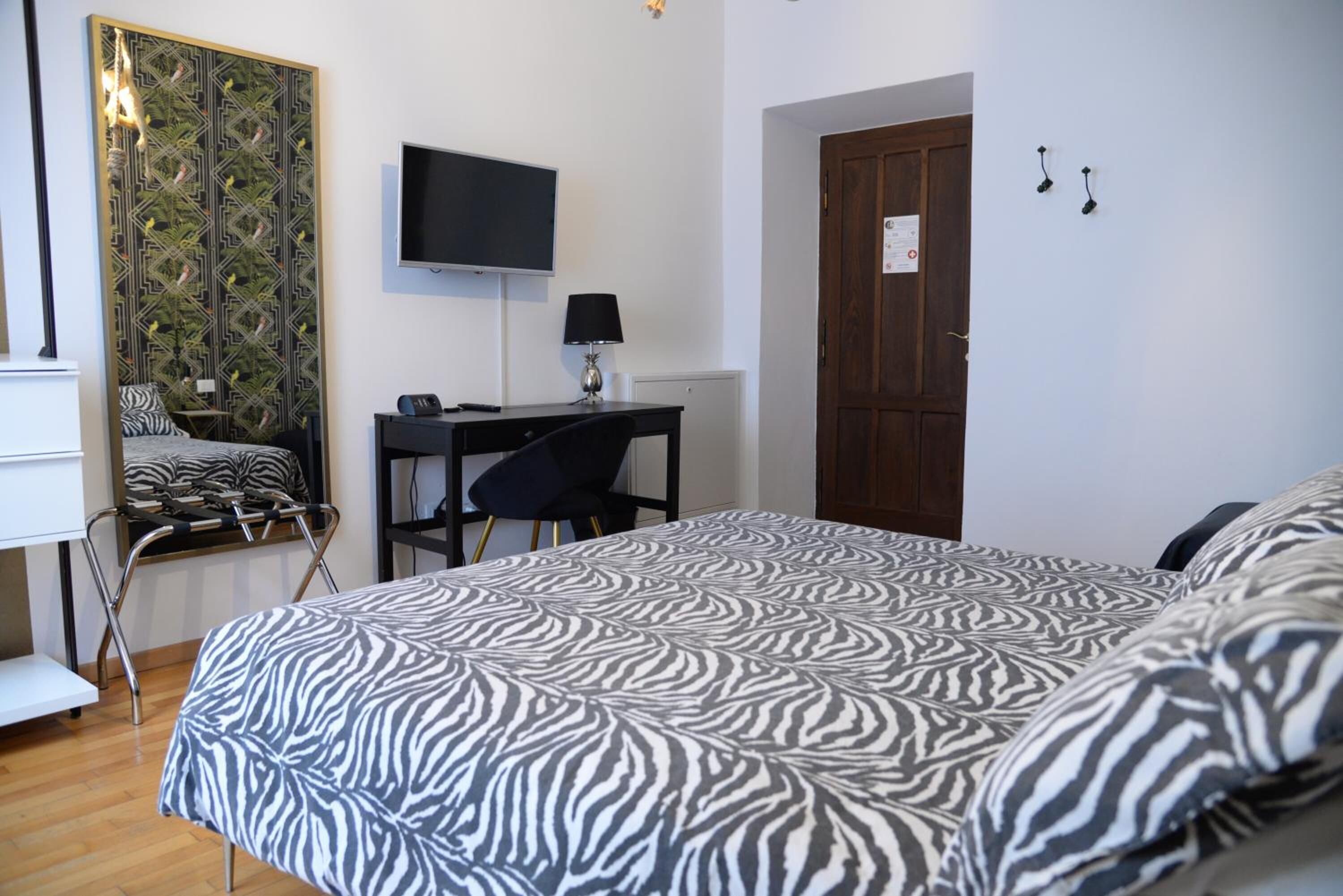 Una camera da letto con copripiumino a motivi zebrati, una scrivania con una sedia, un televisore montato a parete e una porta con un cartello.