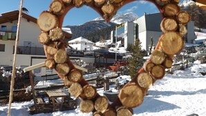 Une décoration en bois en forme de cœur, placée dans un espace extérieur enneigé, avec des bâtiments et des montagnes en arrière-plan.