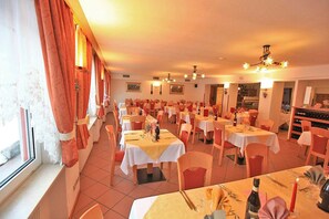 A restaurant with multiple tables and chairs, arranged in rows, with a view of the outside through large windows. - Hotel Vigo (San Giovanni di Fassa)