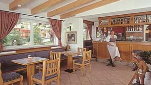 Un restaurant chaleureux avec des poutres en bois, un coin bar et une vue sur l’extérieur par la fenêtre.