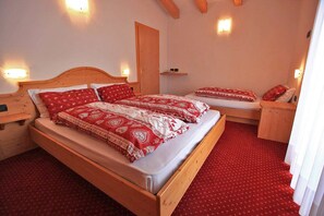 A bedroom with a wooden bed, two bedside tables, a red carpet, and wall-mounted lights. - Hotel Vigo (San Giovanni di Fassa)