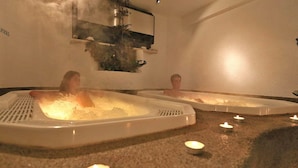 Deux bains à remous fumants, entourés de bougies posées sur un tapis.