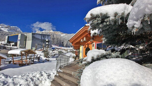 Un espace extérieur enneigé, avec des marches menant à un bâtiment, une structure en bois et des arbres couverts de neige.