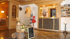 Un espace d’accueil comprenant un comptoir de réception en bois, un panneau d’affichage où sont accrochées diverses informations, une sculpture décorative représentant un lapin et un panneau indicateur avec du texte.