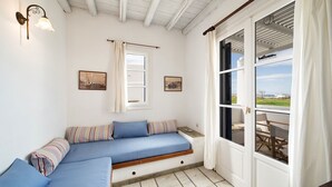 A cozy room with a built-in bench, a window with curtains, and a view of the outdoors. - Brachera Apartments (Paros)