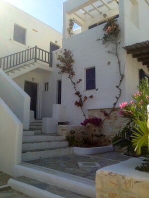 A white building with a staircase leading to a door, a small window, and some plants. - Brachera Apartments (Paros)