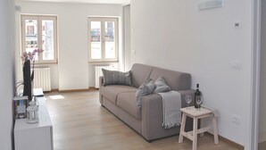 A modern living room with a grey sofa, a small wooden side table, and a radiator. - Casa del Borgo Maria Luisa (Tremosine)