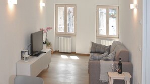 A modern living room with a sofa, a TV, and a small table with a bottle and glass. - Casa del Borgo Maria Luisa (Tremosine)