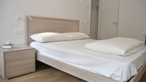 A neatly made bed with white linens, a wooden headboard, and a bedside table with a cup and a book. - Casa del Borgo Maria Luisa (Tremosine)