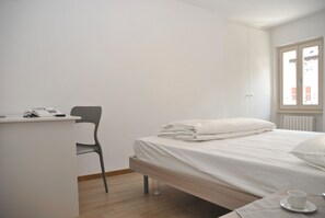 A bedroom with a bed, a desk, a chair, and a window.