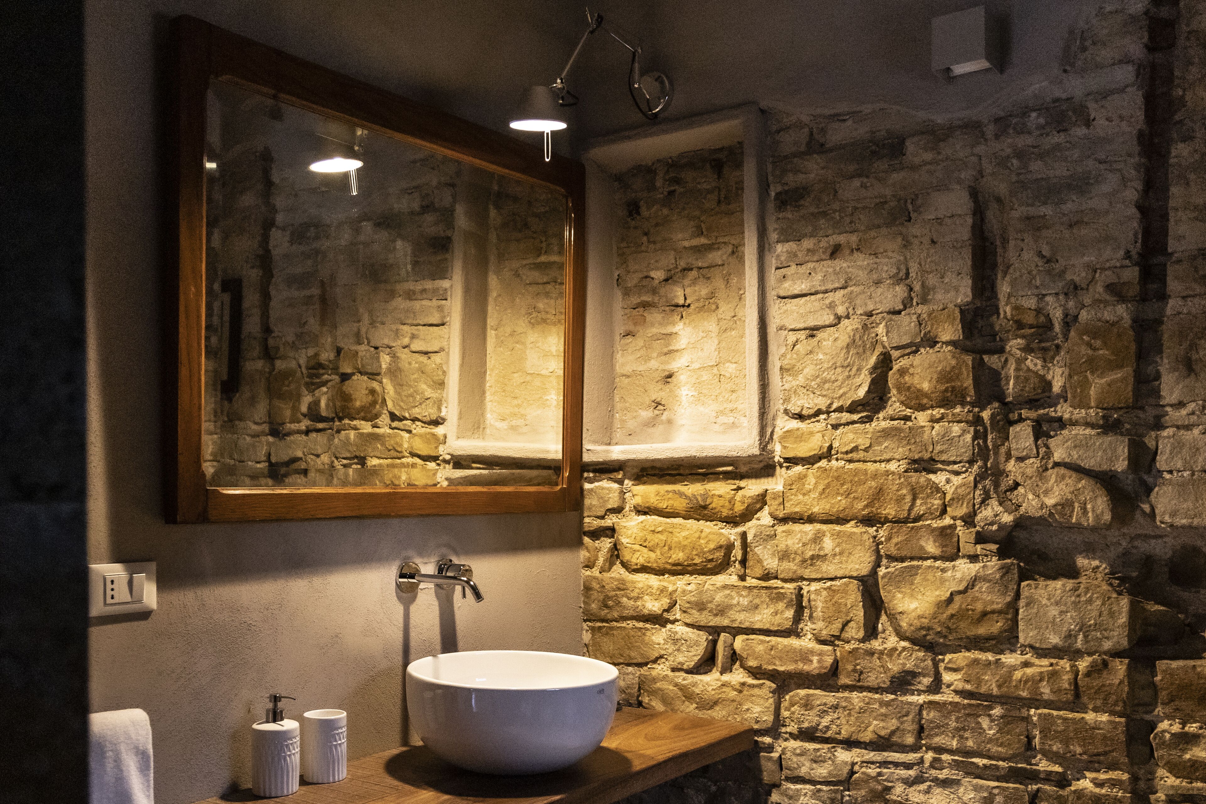 A bathroom with a stone wall, a wooden countertop, a white sink, and a mirror.
