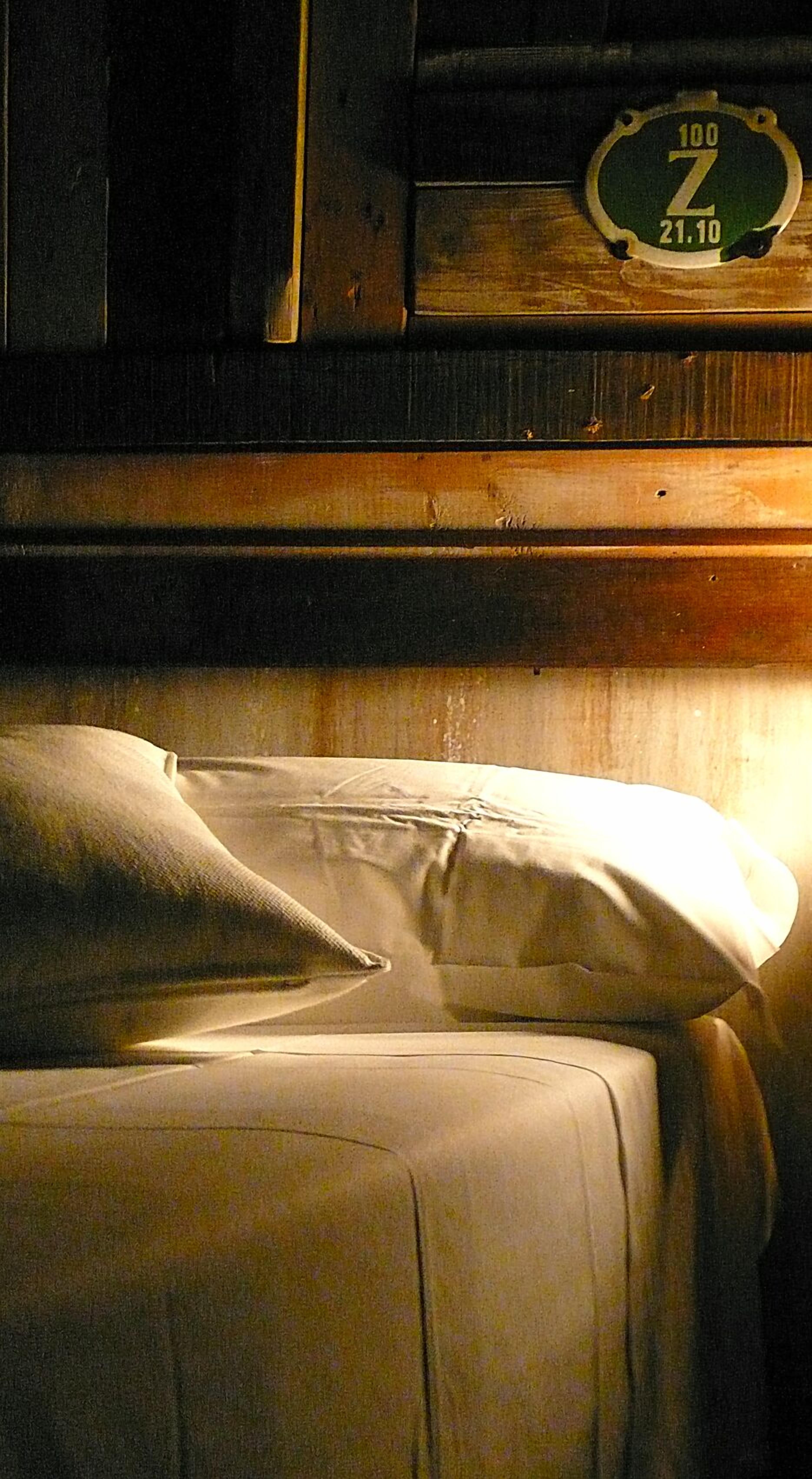 Een kamer met weinig licht, een bed en een houten hoofdeinde, met een klok waarop de tijd staat.