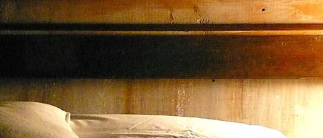 A dimly lit room with a bed, a wooden headboard, and a clock displaying the time.