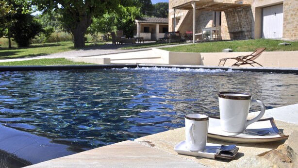 Un cadre agréable au bord de la piscine, avec une table dressée pour deux personnes, comprenant une tasse et une soucoupe, ainsi qu’un plateau avec une cuillère et une autre tasse.