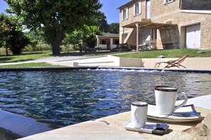 Un cadre agréable au bord de la piscine, avec une table dressée pour deux personnes, comprenant une tasse et une soucoupe, ainsi qu’un plateau avec une cuillère et une autre tasse.