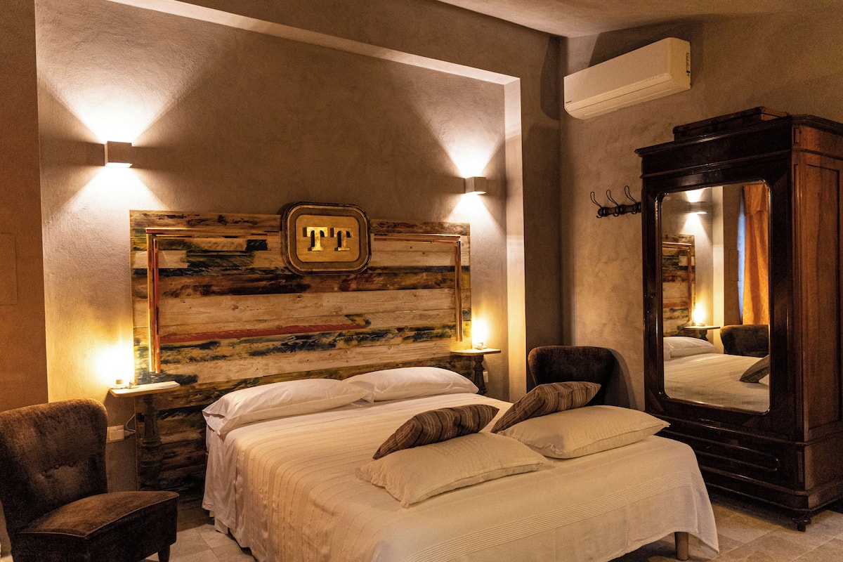 Een hotelkamer met een groot bed, twee nachtkastjes, een stoel, een spiegel en een kunstwerk aan de muur.