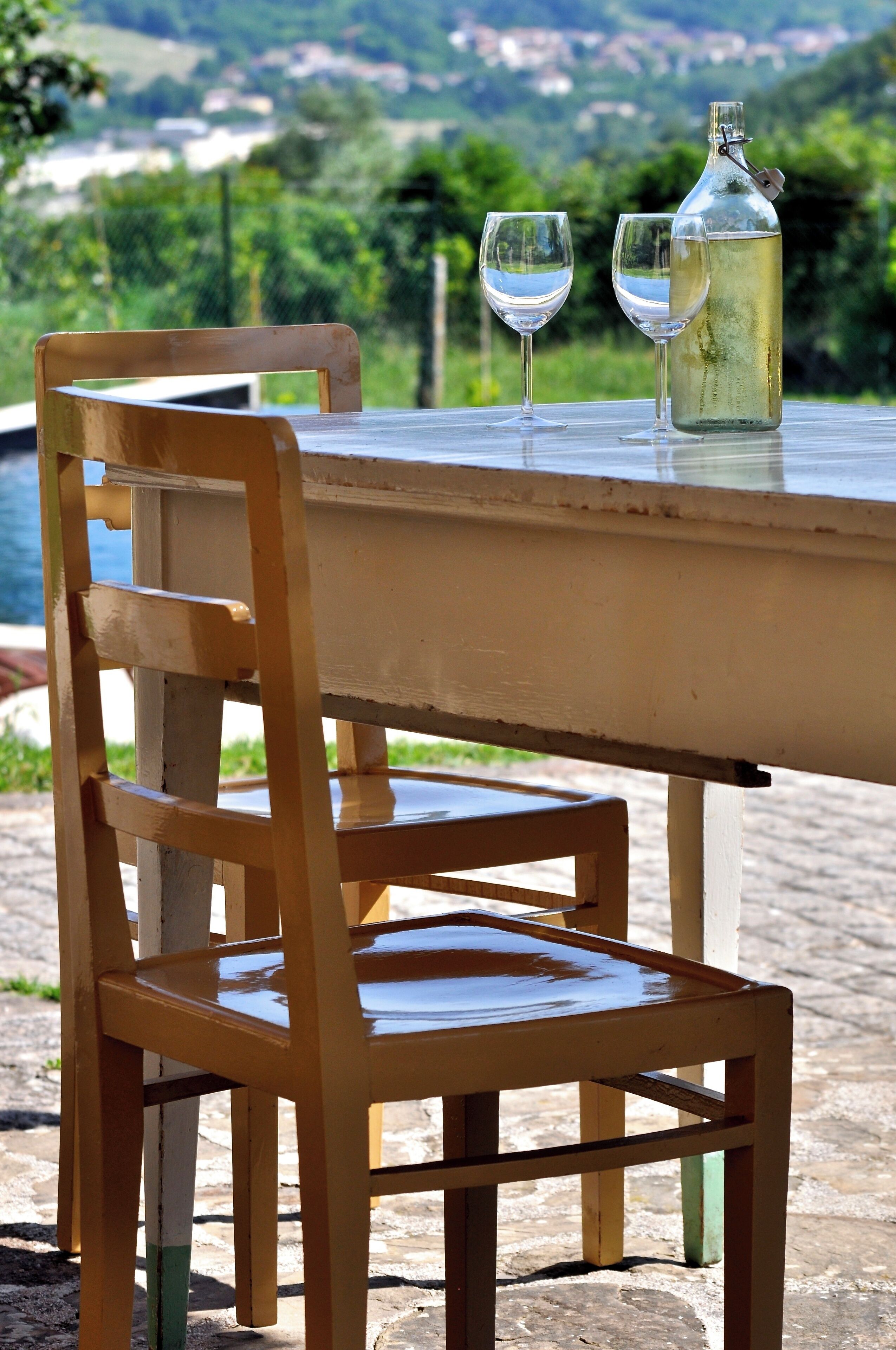 A wooden chair and table with two glasses and a bottle of white liquid.