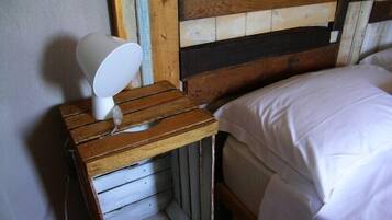 A wooden bedside table with a white lamp, a wooden headboard, and a white bedspread.