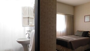 A hotel room with a bed, a bedside table, a window with curtains, a bathroom with a sink and a towel hanging on the wall.