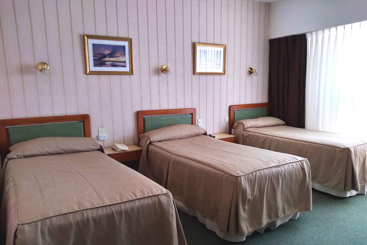 A hotel room with three single beds, a nightstand with a phone, and two framed pictures on the wall.