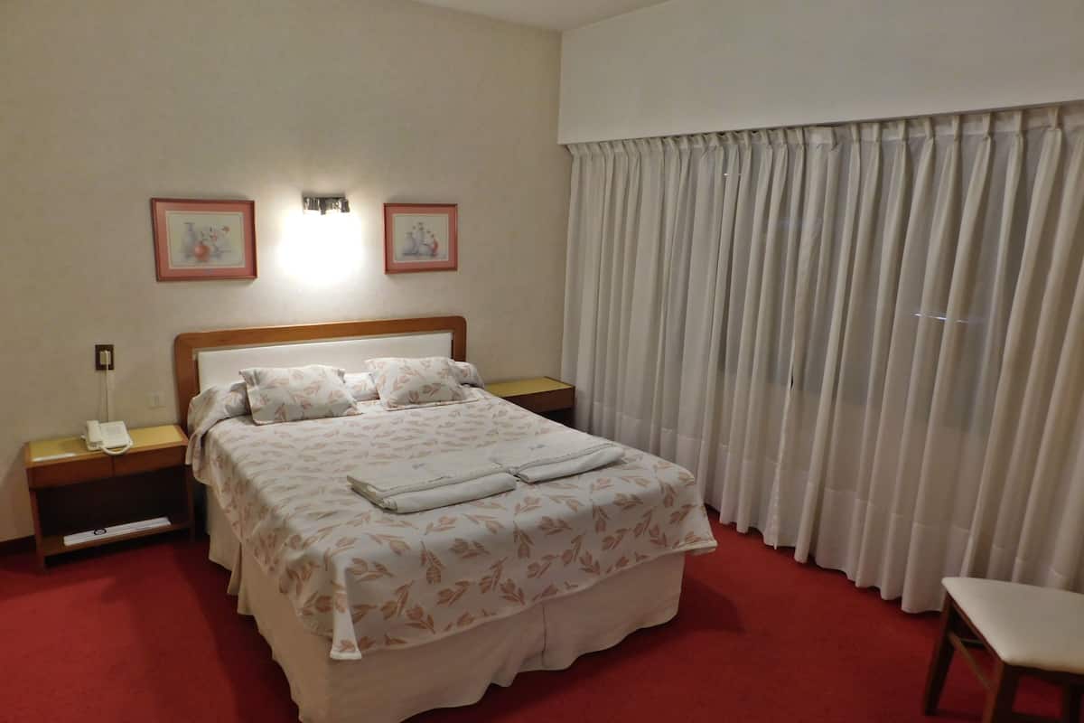 A neatly made bed with a floral bedspread, a bedside lamp, and a nightstand with a phone.