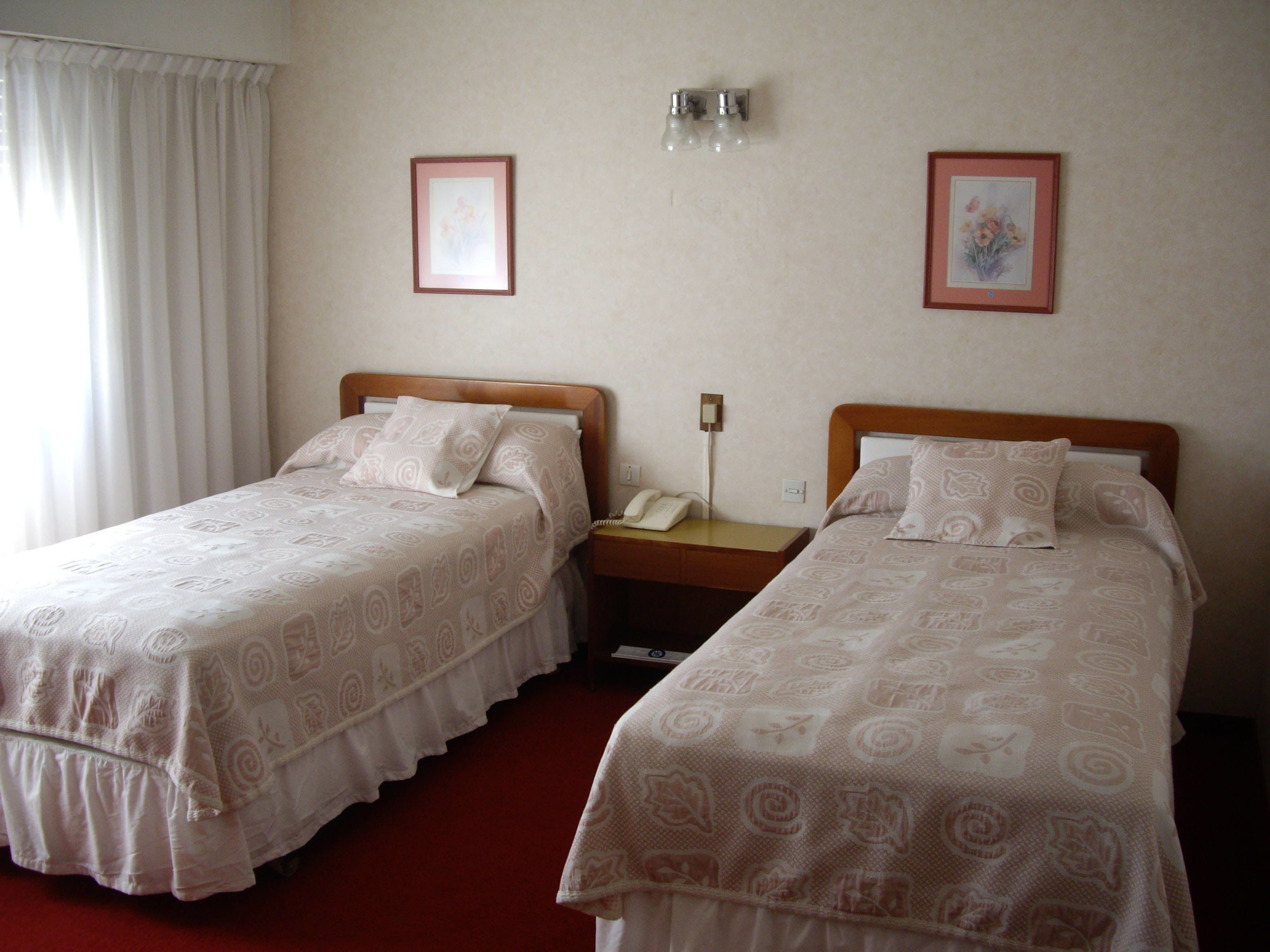 Two single beds with patterned bedding, a bedside telephone, and a wall-mounted light fixture.