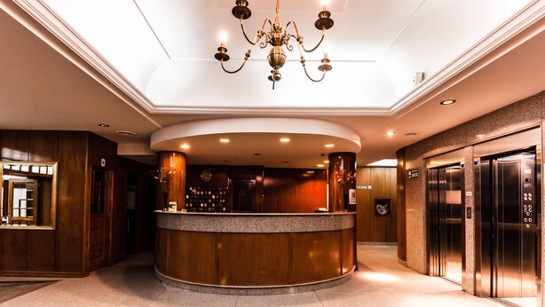 A hotel lobby with a reception desk, a chandelier, and an elevator.