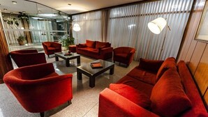 A modern living room with red sofas and armchairs, a coffee table, and a large window with curtains.