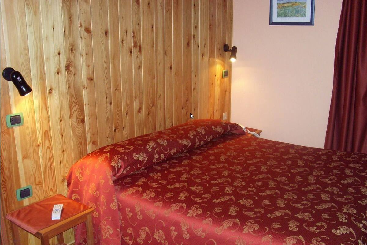 Ein Zimmer mit Holzwänden, einem Bett, einem kleinen Tisch und einer Wandlampe.