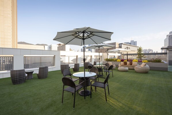 Une terrasse sur le toit avec des espaces de détente en plein air, comprenant des tables et des chaises rondes, ainsi que des parasols.