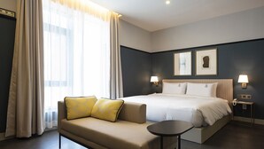 Hotellihuone, jossa on sänky, sohva, pieni pöytä ja kaksi seinälle asennettua lamppua.