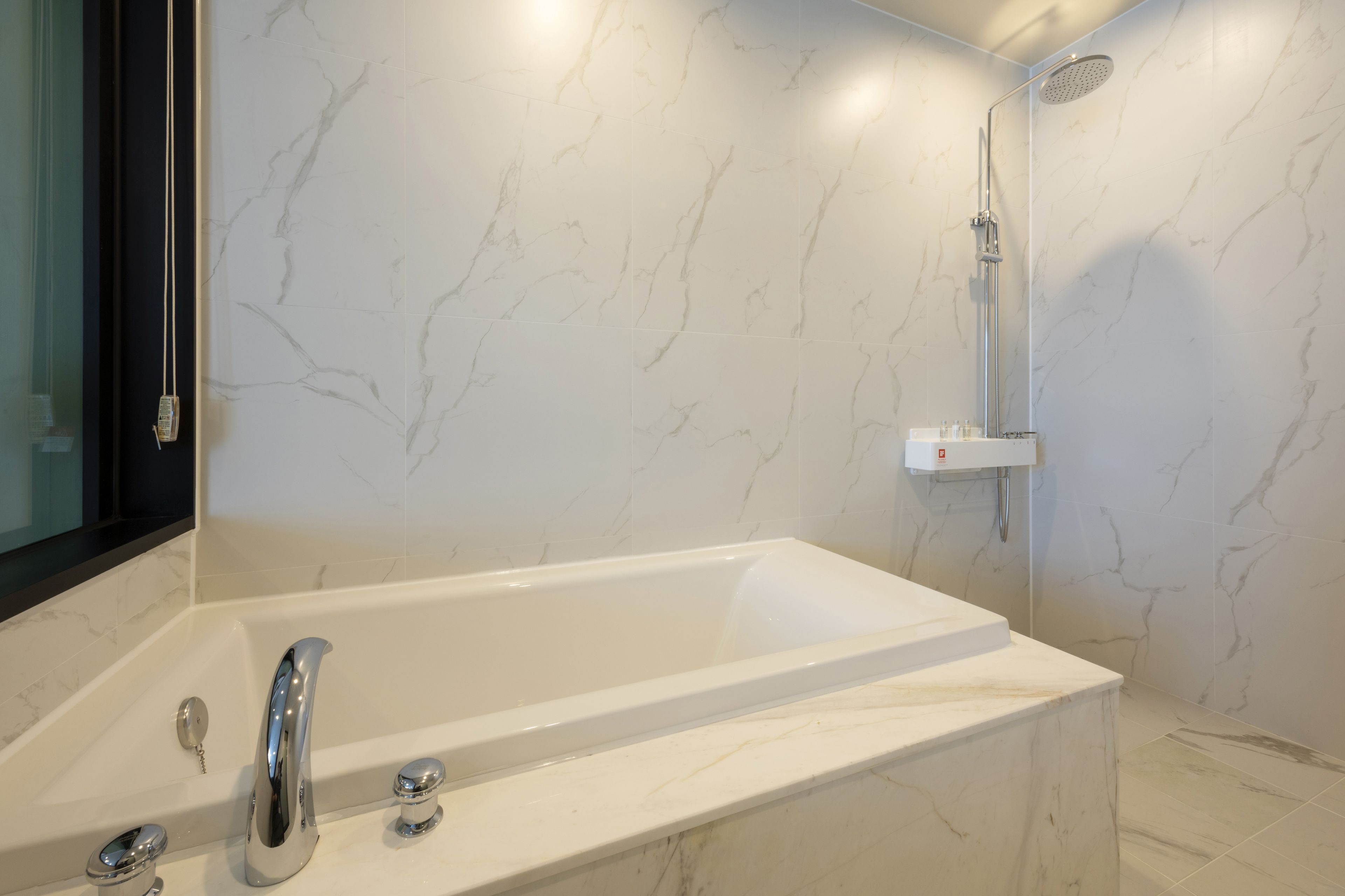 A modern bathroom with a marble-tiled wall, a freestanding bathtub, a showerhead, and a mirror.