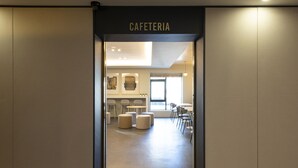 Moderni sisustus, jossa on näkyvillä kyltti, jossa lukee ”CAFETERIA”. Tilan suunnittelussa on käytetty minimalistista tyyliä, ja siinä on keskeinen oleskelualue sekä näkymä ulos.