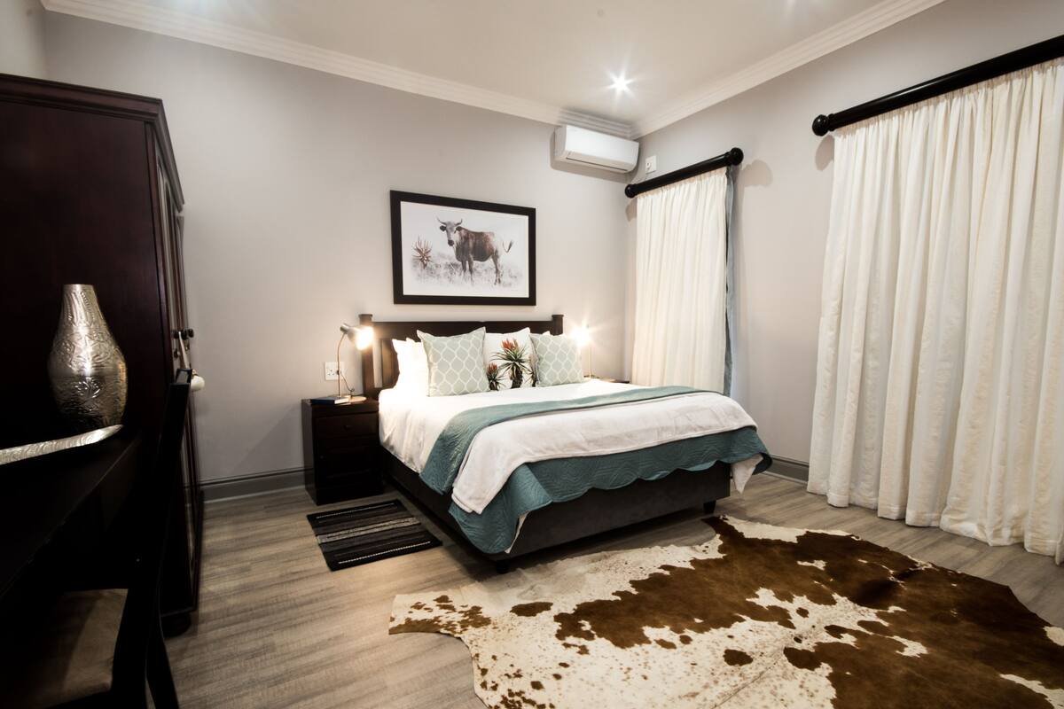 A bedroom with a bed, bedside tables, a decorative vase, a framed picture, and a cowhide rug.
