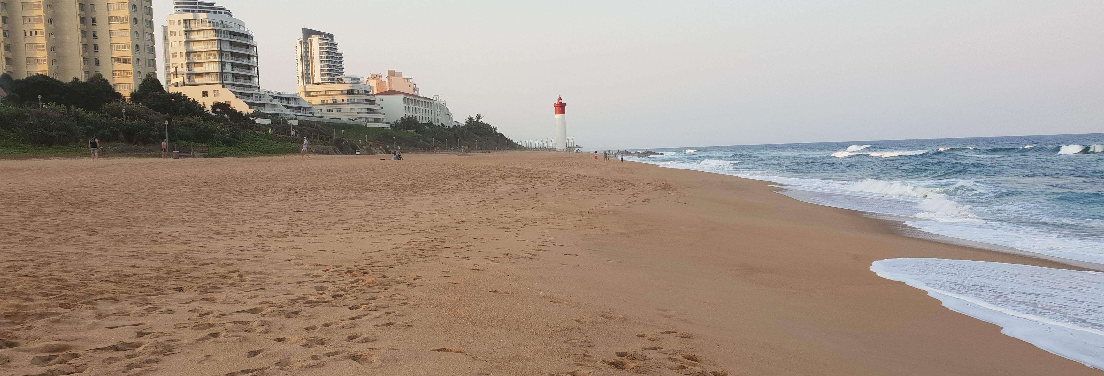 Een strand met voetafdrukken, een vuurtoren en gebouwen op de achtergrond.
