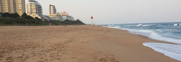 Una playa con huellas, un faro y edificios al fondo.