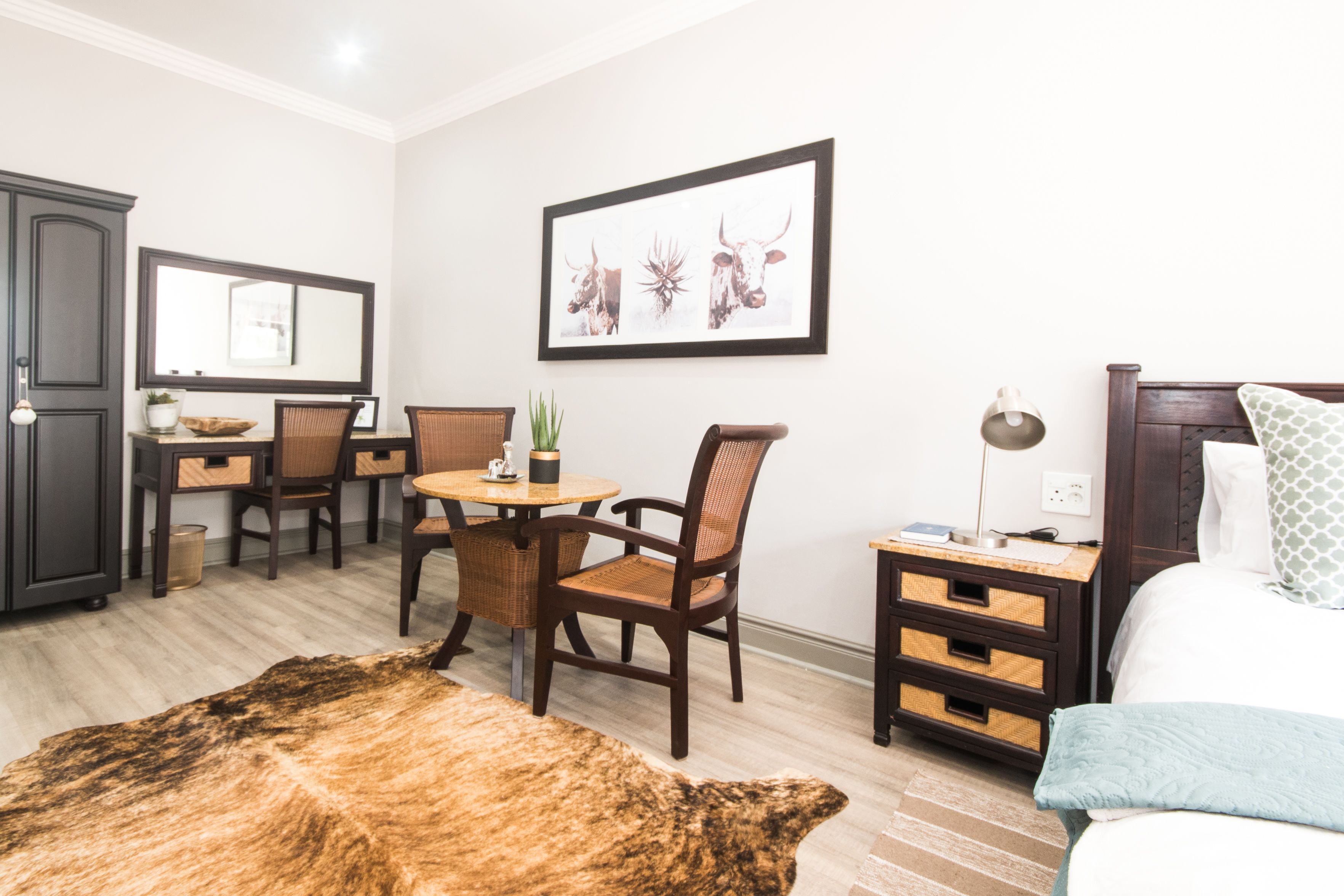 Habitación de hotel con cama, escritorio con sillas, mesa de comedor, alfombra y un cuadro en la pared.