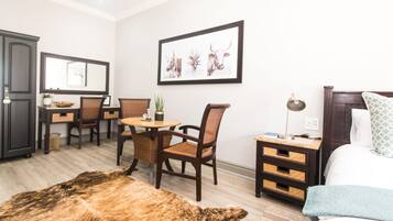 Habitación de hotel con cama, escritorio con sillas, mesa de comedor, alfombra y un cuadro en la pared.
