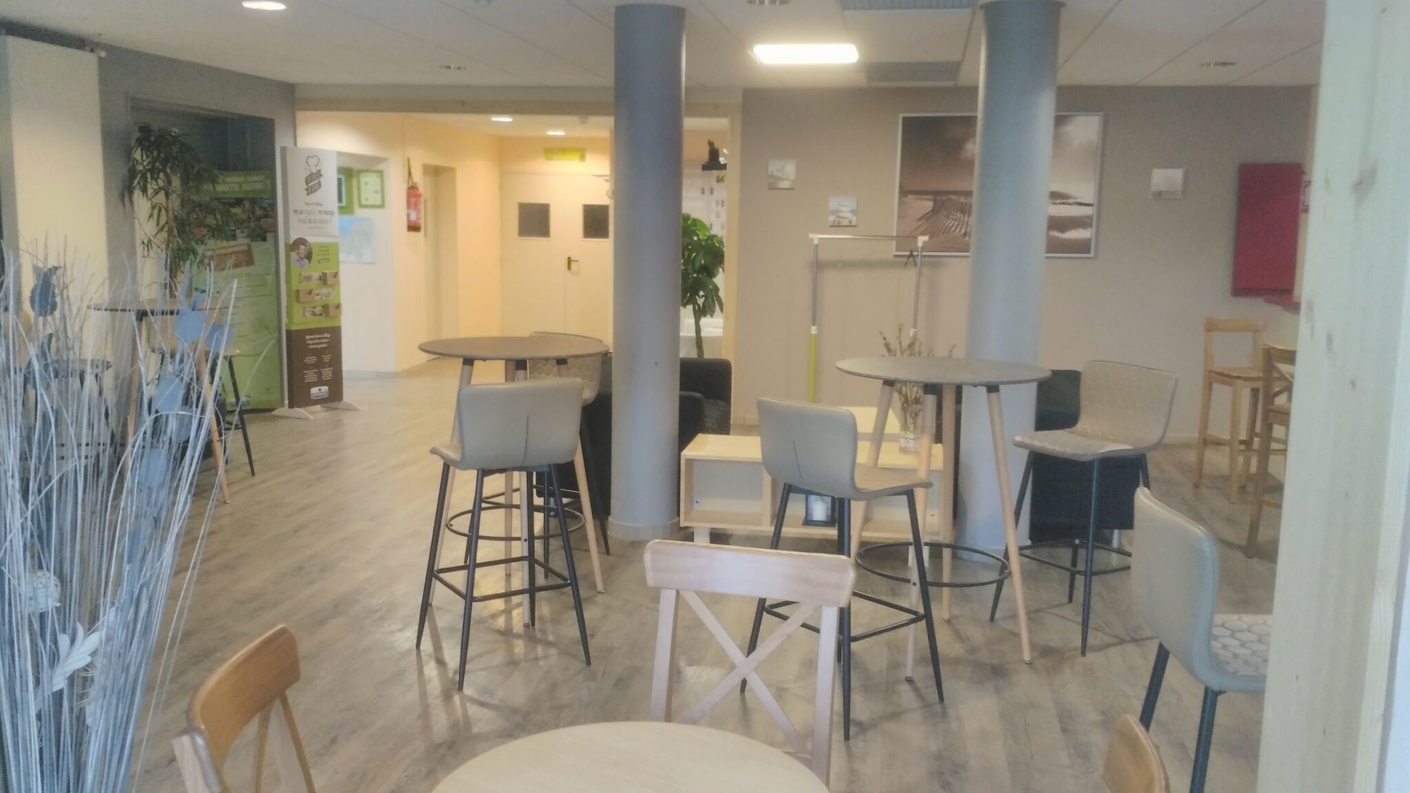 Un interno moderno con diverse zone di seduta, tra cui tavoli e sedie rotonde, e un pilastro centrale.